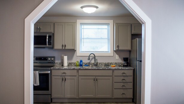 A compact kitchen with a built-in microwave, oven, and refrigerator. It features a window with blinds, a sink with a faucet, and a countertop with dish soap and a sponge. - Holland Suites, Suite #4 (Williamstown)