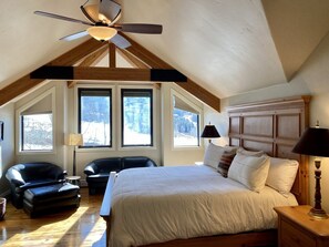 A bedroom with a large bed, two chairs, a ceiling fan, and a view of the outdoors. - 226 Country Club Dr 5 Bedroom House (Mountain Village)