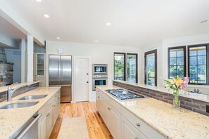 A modern kitchen with stainless steel appliances, a granite countertop, and large windows.