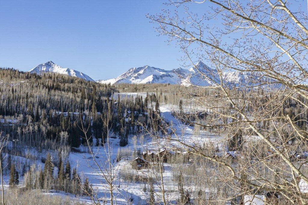 A mountainous landscape with snow-covered peaks, a forested area, and a small cabin.