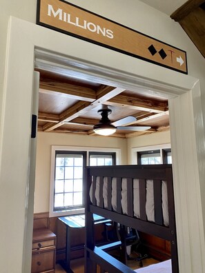A room with a ceiling fan, wooden beams, a desk, and a chair.
