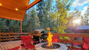 A wooden deck with a fire pit, red chairs, and a grill. - 3 Story Cabin w/Spacious Deck and a Treasure Hunt (Duck Creek Village)