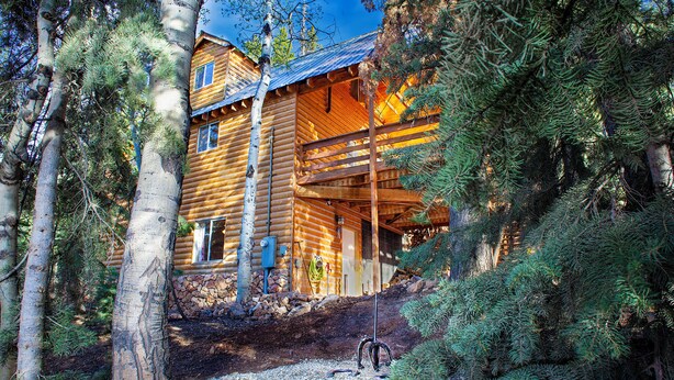 A log cabin with a wooden porch, surrounded by trees and a stone wall. - 3 Story Cabin w/Spacious Deck and a Treasure Hunt (Duck Creek Village)