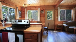 A cabin interior with a kitchen area, wooden flooring, a dining table, and a sofa. - 3 Story Cabin w/Spacious Deck and a Treasure Hunt (Duck Creek Village)