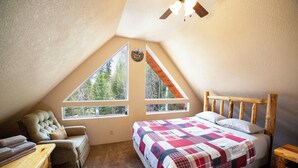 A bedroom with a large window, a wooden bed, a chair, and a small table. - 3 Story Cabin w/Spacious Deck and a Treasure Hunt (Duck Creek Village)