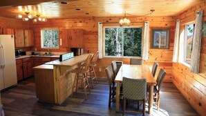 A wooden cabin interior with a kitchen, dining area, and large windows. - 3 Story Cabin w/Spacious Deck and a Treasure Hunt (Duck Creek Village)