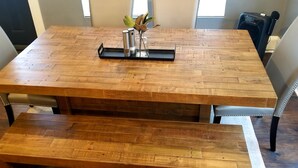 Une table de salle à manger en bois, sur laquelle se trouvent un plateau noir, des salières et des poivrières, ainsi qu'un vase avec des fleurs.