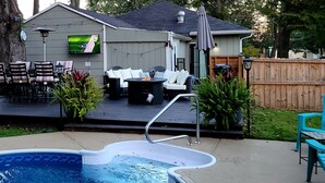 Un jardin avec une piscine, un barbecue, un coin salon extérieur et un téléviseur fixé au mur.