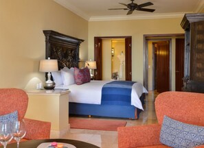 Quarto de hotel com cama, duas mesas de cabeceira, um criado-mudo, uma cadeira, uma mesa com um copo e um ventilador de teto.