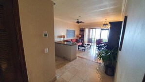 A spacious living area with a sofa, coffee table, and a dining table with chairs. There is a ceiling fan and a chandelier.