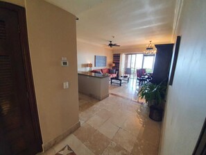 Ampla sala de estar com sofá, mesa de centro e mesa de jantar com cadeiras. Há um ventilador de teto e um lustre.