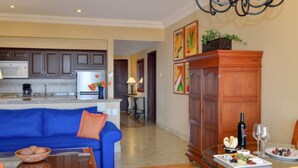 A modern kitchen with dark cabinets, a white microwave, and a coffee maker. There is a blue sofa with orange cushions in the living area, and a dining table set with plates of food and wine glasses.