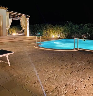 Una piscina amb un solàrium d'rajola, una cadira de gandules i una zona coberta amb cortines.