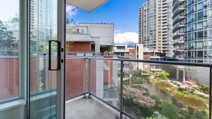 Un balcon doté d’une porte vitrée, donnant sur un jardin aménagé et les bâtiments adjacents.