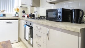 Een moderne keuken met witte kasten, een zwarte magnetron, een koffiezetapparaat en een gasfornuis.