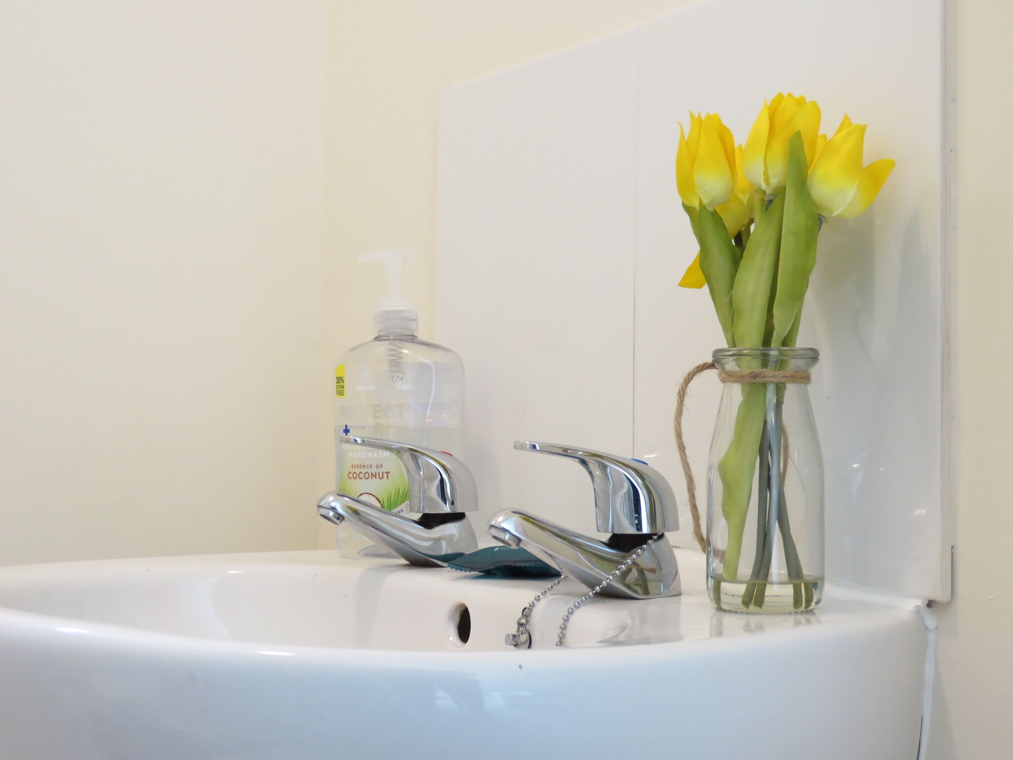 Un lavabo de salle de bain avec un distributeur de savon liquide et un vase contenant des fleurs jaunes.