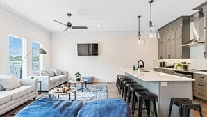 Cozinha moderna com ilha central, banquetas e área de jantar com sofá e mesa de centro.