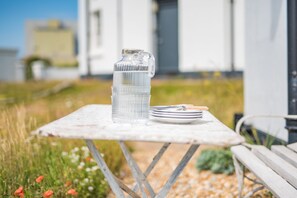 A clear glass water bottle and a stack of plates on a white table outdoors.