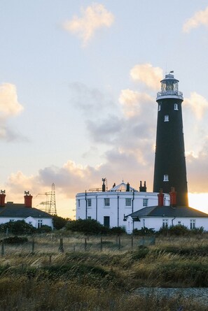 A lighthouse with a white building in front, surrounded by grass and a fence.