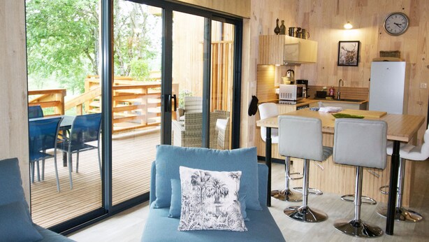 A modern kitchen with wooden cabinets, a dining area with bar stools, and a large sliding glass door leading to an outdoor deck. - HOUSE WITH AIR CONDITIONING (Doucier)