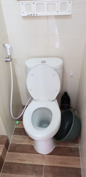 Een toilet met een douchetoilet, een groene schoonmaakfles en een zwarte container op de vloer.