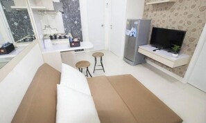 A compact living space with a kitchenette, a sofa, two stools, a television, and a refrigerator. - Apartment Green Pramuka by Vincent by Zuzu (Jakarta)