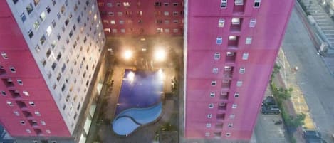Ein Hochhaus mit mehreren Etagen, einem Pool auf dem Dach und einem Parkplatz darunter.