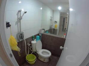 Une salle de bain avec des toilettes, une douche, un miroir et un seau vert.
