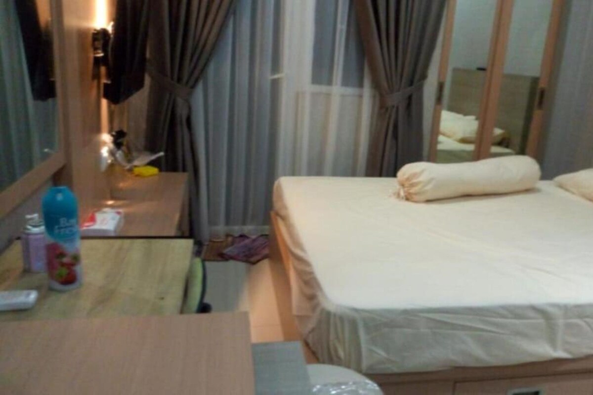 Een hotelkamer met een bed, een bureau met stoel, een spiegel en een raam met gordijnen.