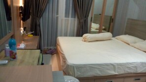 Een hotelkamer met een bed, een bureau met stoel, een spiegel en een raam met gordijnen.