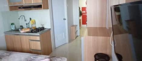 Ein kleines Hotelzimmer mit Bett, Fernseher, Küchenzeile und Bad.