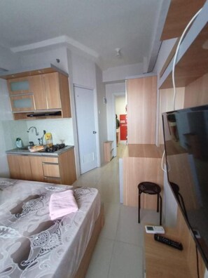 Ein kleines Hotelzimmer mit Bett, Fernseher, Küchenzeile und Bad.