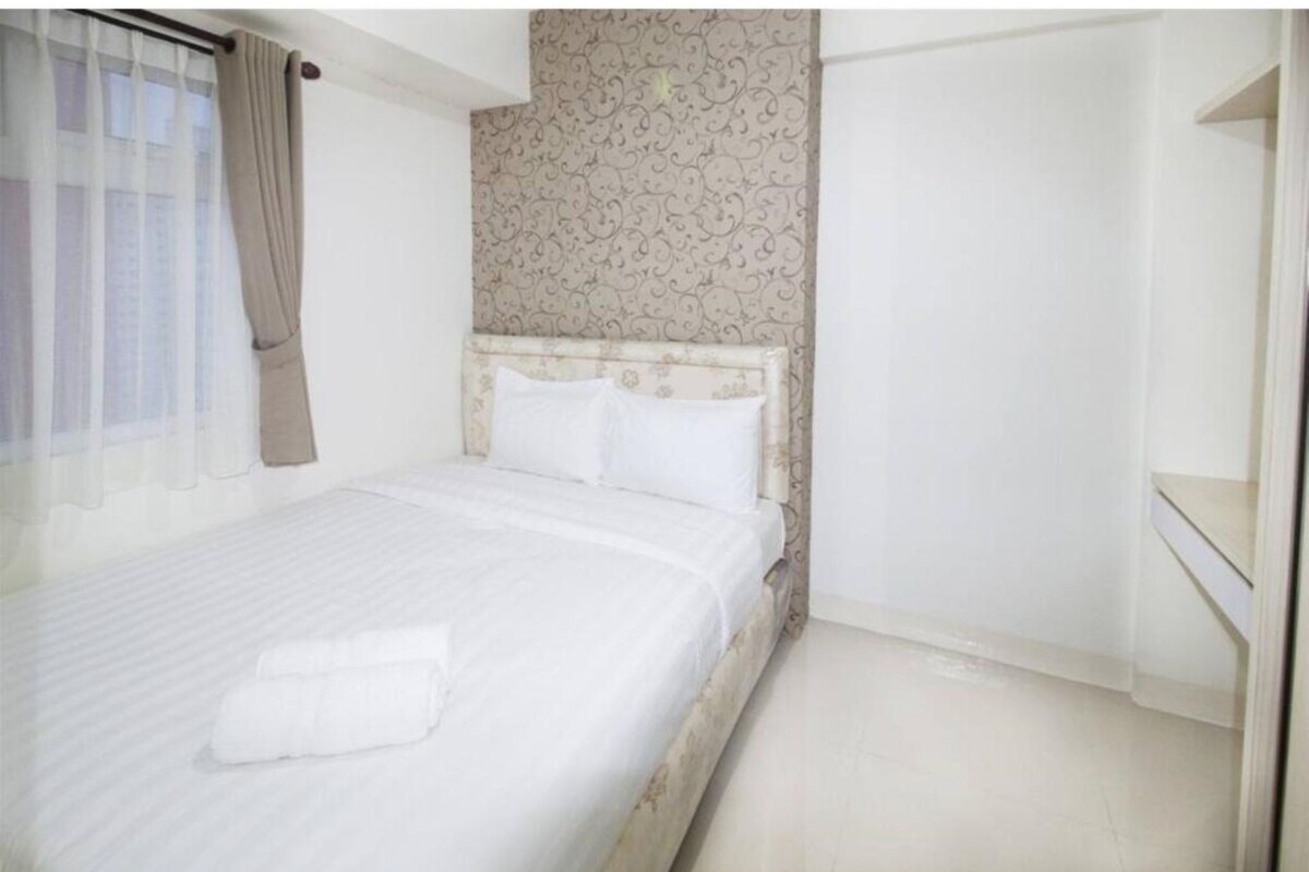 Une chambre à coucher avec un lit, une tête de lit, une fenêtre avec des rideaux et un mur décoré d’un motif.