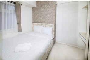 Une chambre à coucher avec un lit, une tête de lit, une fenêtre avec des rideaux et un mur décoré d’un motif.
