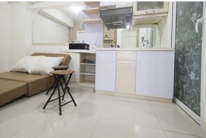 Een compacte leefruimte met een bank, een klein tafeltje, een kitchenette en een decoratieve wand.