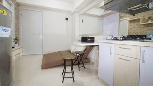 Eine kompakte Küche mit Kühlschrank, Herd und Spüle. Dazu ein kleiner Sitzbereich mit einer Couch und zwei Hocker.