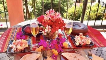 Una mesa dispuesta al aire libre con platos de comida, copas de vino y un jarrón de flores.