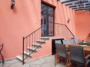 A dining area with a table set for two, a staircase, and a window with metal bars.