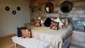A bedroom with a large bed, a bench, and a wooden wall with mirrors and circular decorations. - Departamento Villa Neek (San Cristóbal de las Casas)