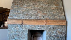 A stone fireplace with a wooden mantel, a woven rug, and two ottomans. - Departamento Villa Neek (San Cristóbal de las Casas)