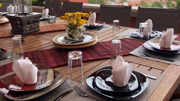 A dining table set for four with plates, cutlery, and napkins, overlooking a scenic view of a town and mountains. - Departamento Villa Neek (San Cristóbal de las Casas)