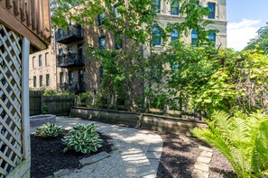 A courtyard with a wooden fence, a gravel path, and a variety of plants. - Stunning Vintage/Modern Brady St Home! Very Walkable, Deck, Fire Pit, Great Find (Milwaukee)