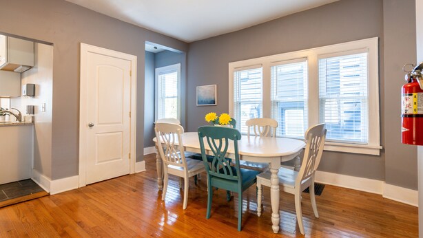 A dining area with a white table and chairs, a small vase with yellow flowers, and a fire extinguisher mounted on the wall. - Stunning Vintage/Modern Brady St Home! Very Walkable, Deck, Fire Pit, Great Find (Milwaukee)