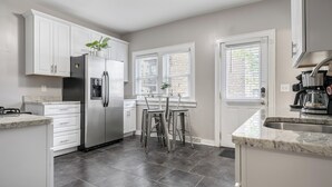 A modern kitchen with white cabinets, a stainless steel refrigerator, a coffee maker, and a dining area with a table and chairs.