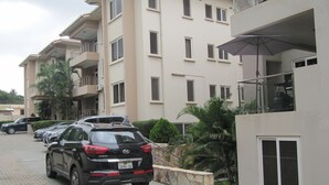 Un edificio residencial de varios pisos con balcones, un estacionamiento con varios coches y un paraguas grande a la derecha.