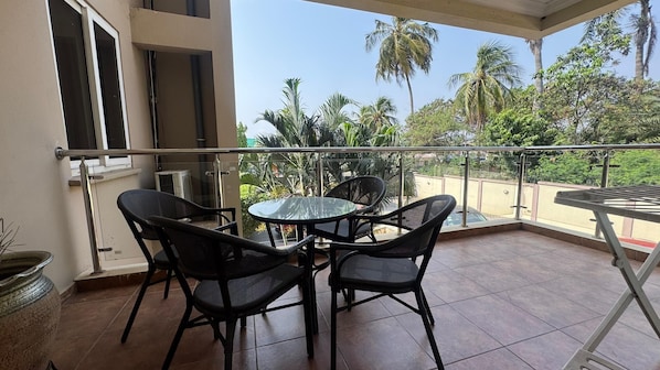 A balcony with a glass railing, a round table, and four chairs.