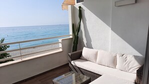 A balcony with a wicker sofa and a small table, overlooking a beach with calm waters and a clear sky. - Apartment in front of the beach and with free parking in the same building. (Altea)