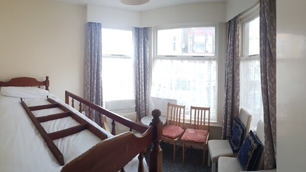 A bedroom with a wooden bed, a chair, and a window with curtains.