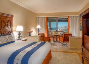 Quarto de hotel com uma cama grande, área de refeições com cadeiras, mesa e vista para o mar.