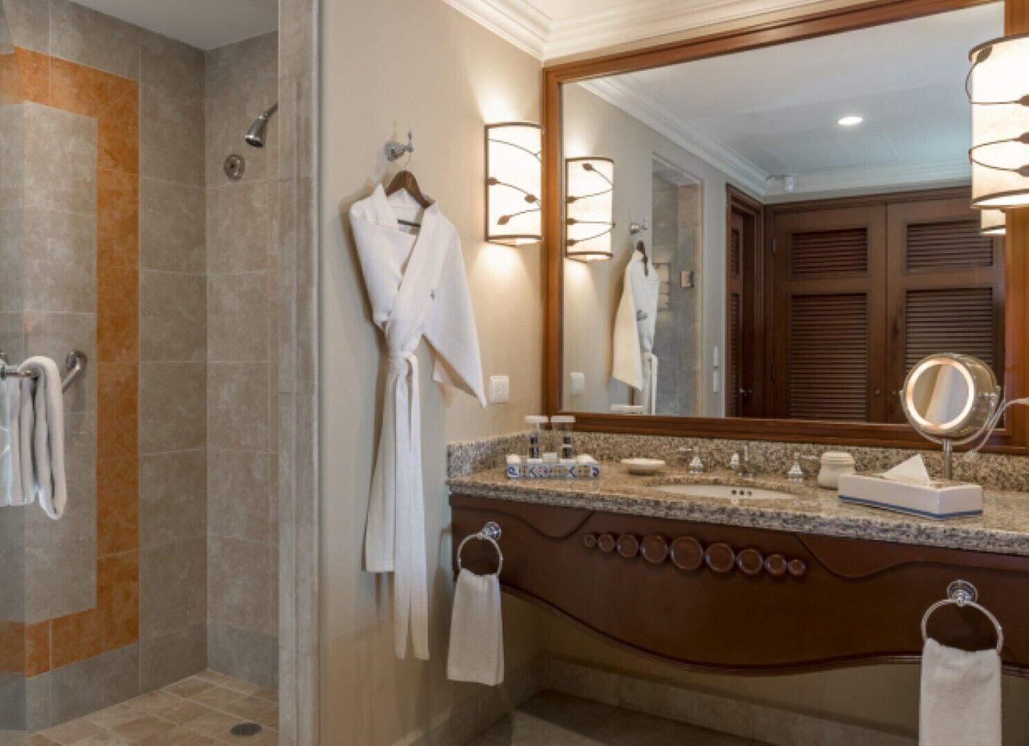 Une salle de bain dotée d’une douche à l’italienne, d’un grand miroir et d’un meuble-lavabo avec un plan de travail en granit.